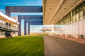 A grassy area beside a building features a wooden bench, inviting relaxation in a serene outdoor setting.