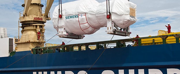 A large cargo ship is being loaded with a substantial object at a bustling port.