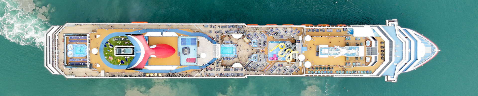 Aerial view of a large cruise ship sailing through the deep blue ocean, surrounded by gentle waves and sunlight reflections.